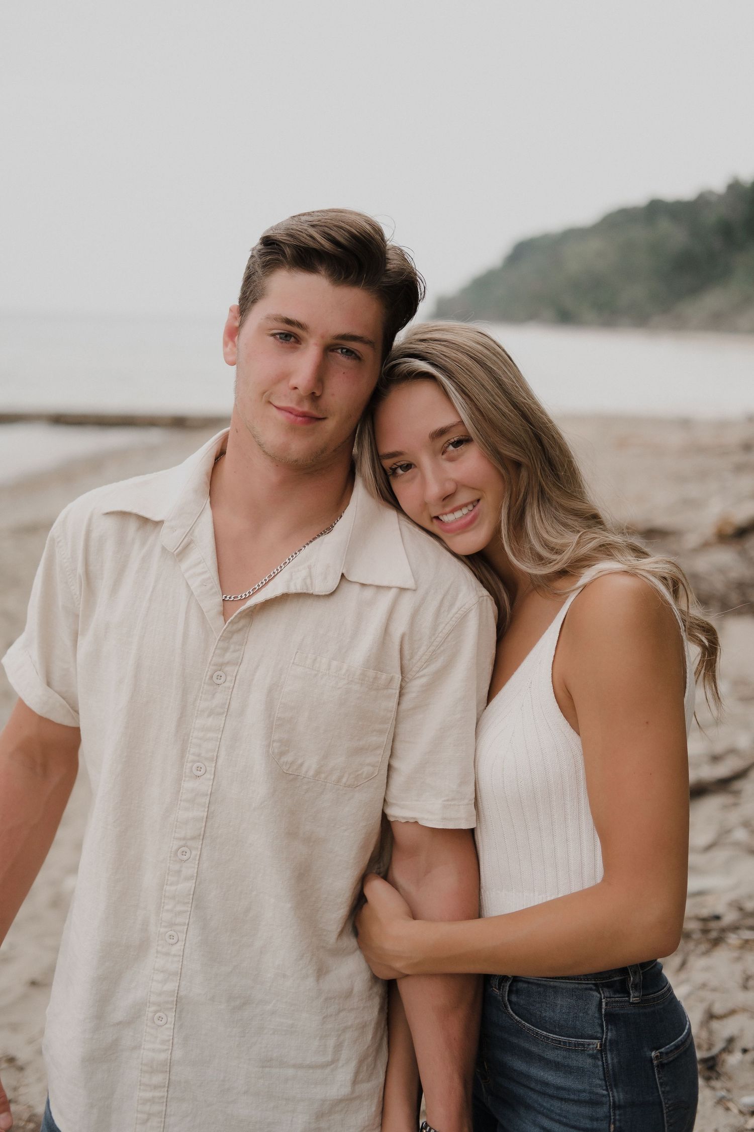 Couple in light colored clothing embracing on a beach during a photo session.