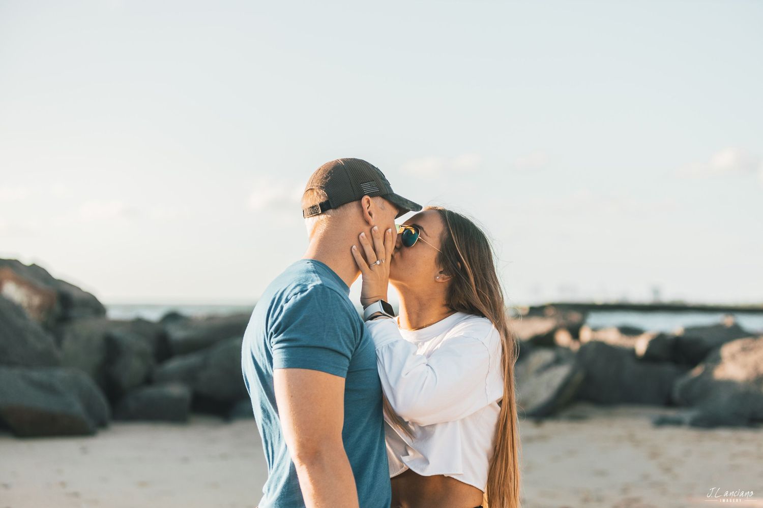 Romantic couple sharing an intimate moment on a rocky beach at sunset.