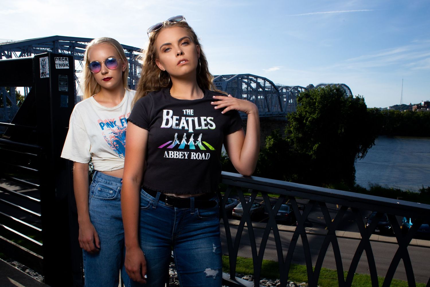 Two people posing on bridge with industrial background at dusk.