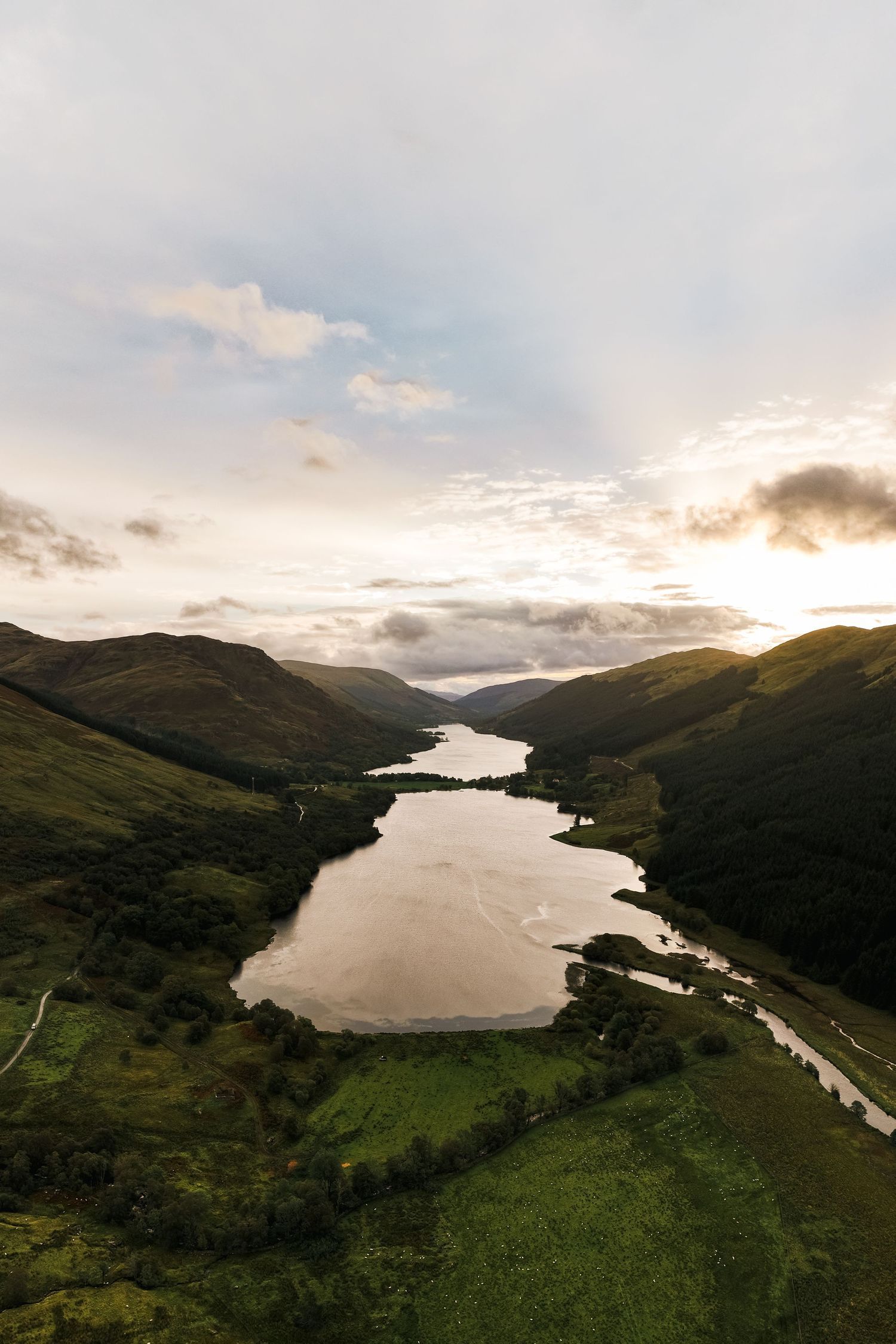 Panoramic aerial view of a serene lake surrounded by green mountains at sunset.
