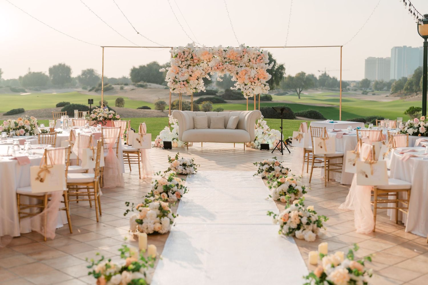 Elegant outdoor wedding reception setup with floral arch and centerpieces on white tables overlooking a golf course.