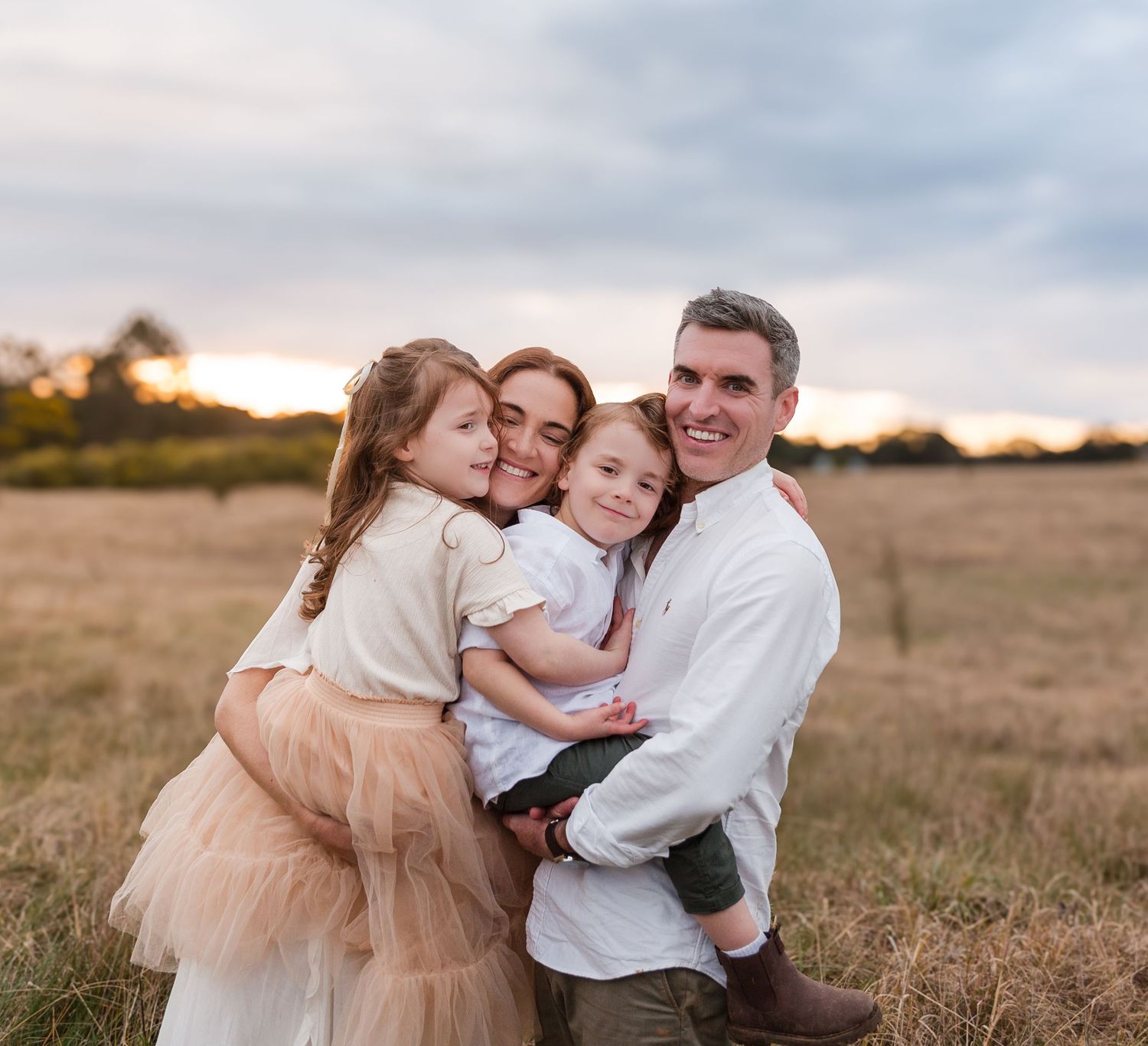 Family embracing and sharing intimate moments in rustic field at sunset.