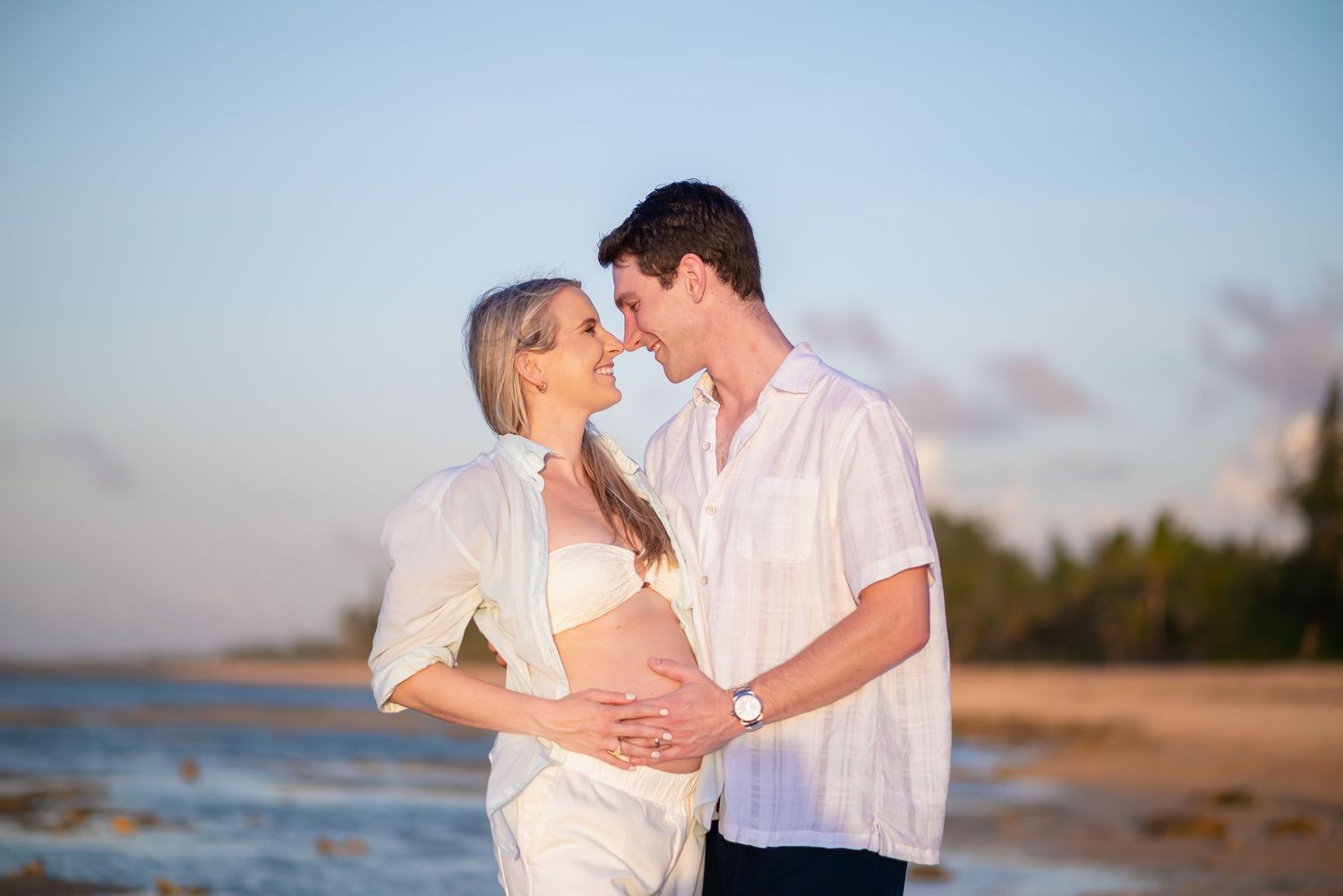 Romantic maternity beach portrait with couple in white at sunset.
