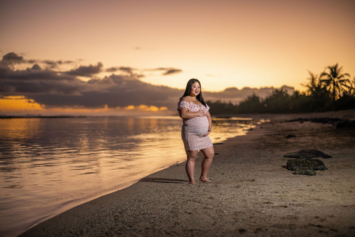 Sunset maternity photo on tropical beach with palm trees and golden sky.
