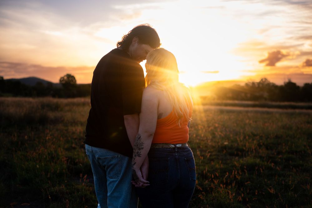 Silhouetted couple sharing intimate moment at golden sunset in countryside.