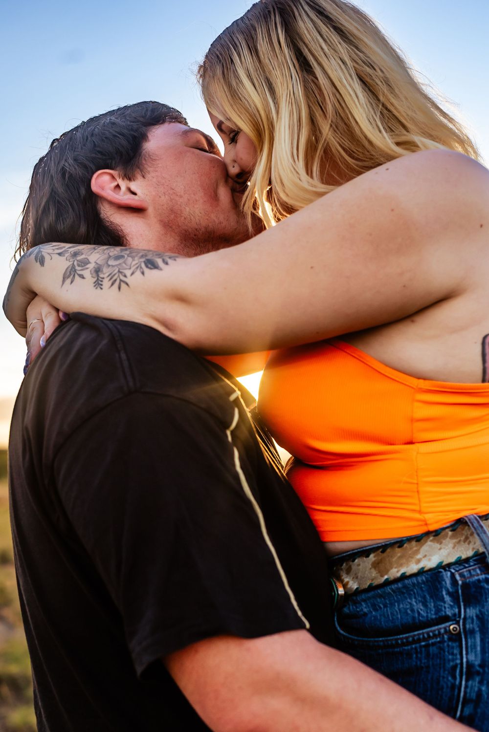 Close-up of couple sharing passionate kiss at sunset with warm golden lighting.