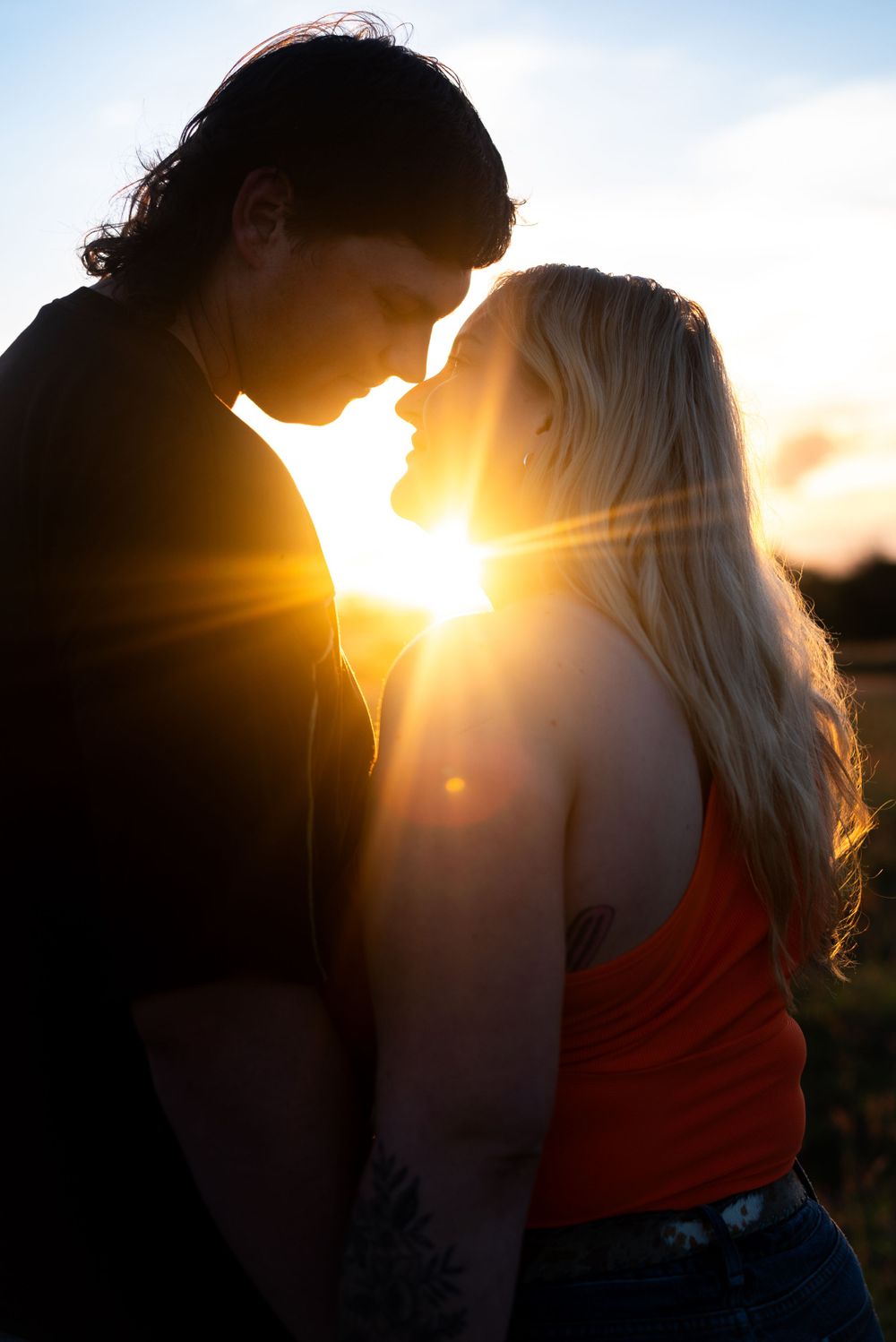 Silhouetted couple shares an intimate moment as sun rays burst through creating a romantic backlit scene.