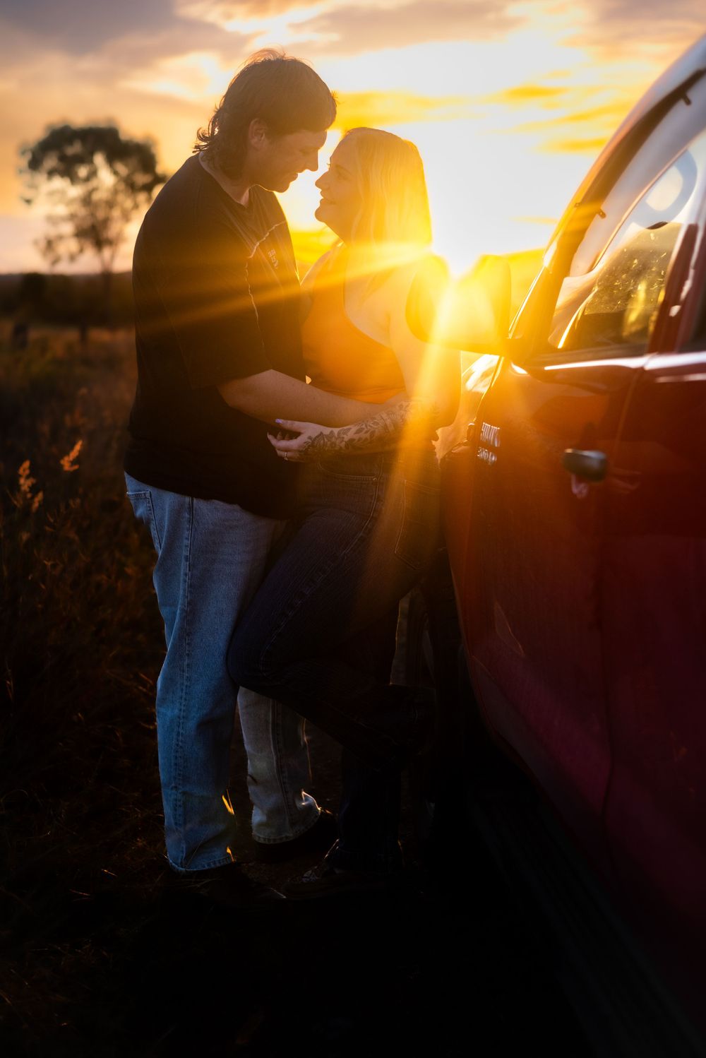 Couple sharing a romantic sunset moment next to their car in a rural setting.