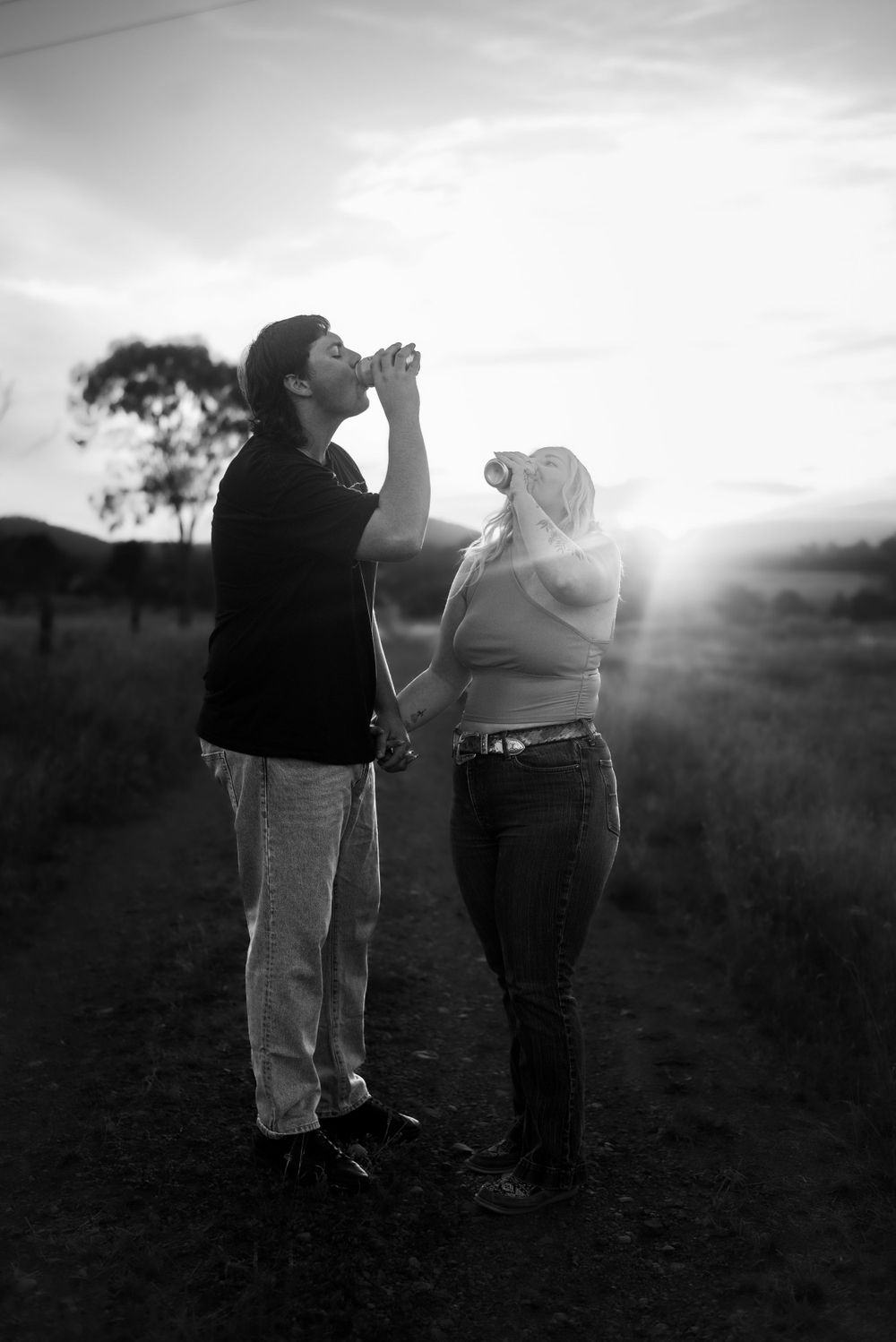 Black and white photo of playful couple making silly gestures together at sunset.