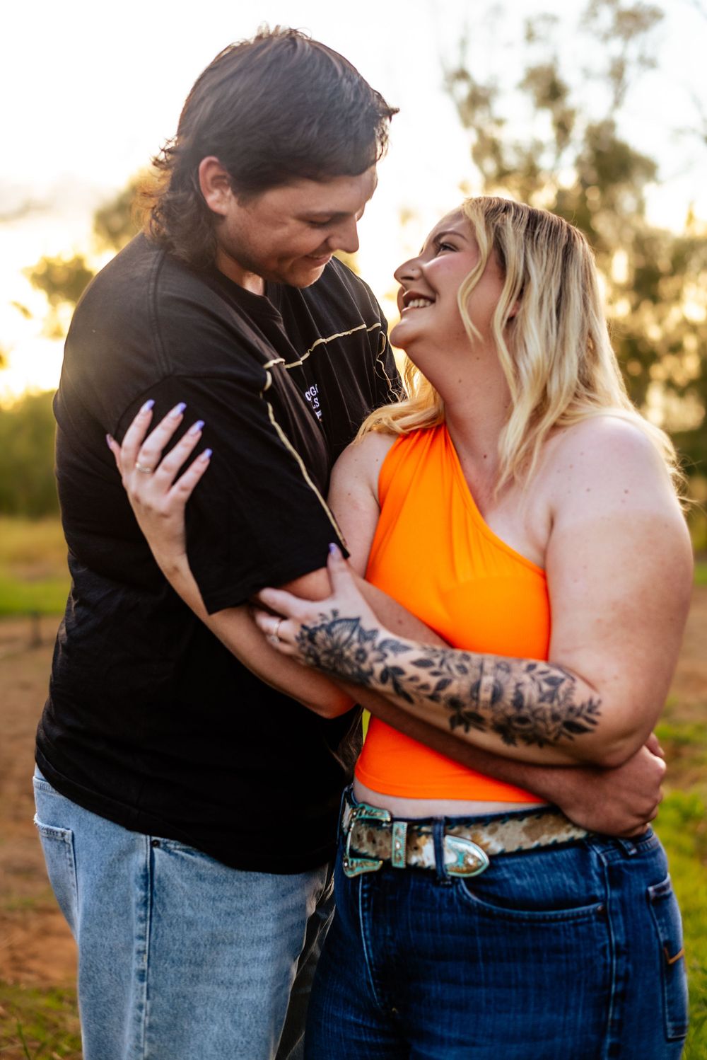 Couple laughing together in warm evening sunlight while sharing an intimate embrace outdoors.