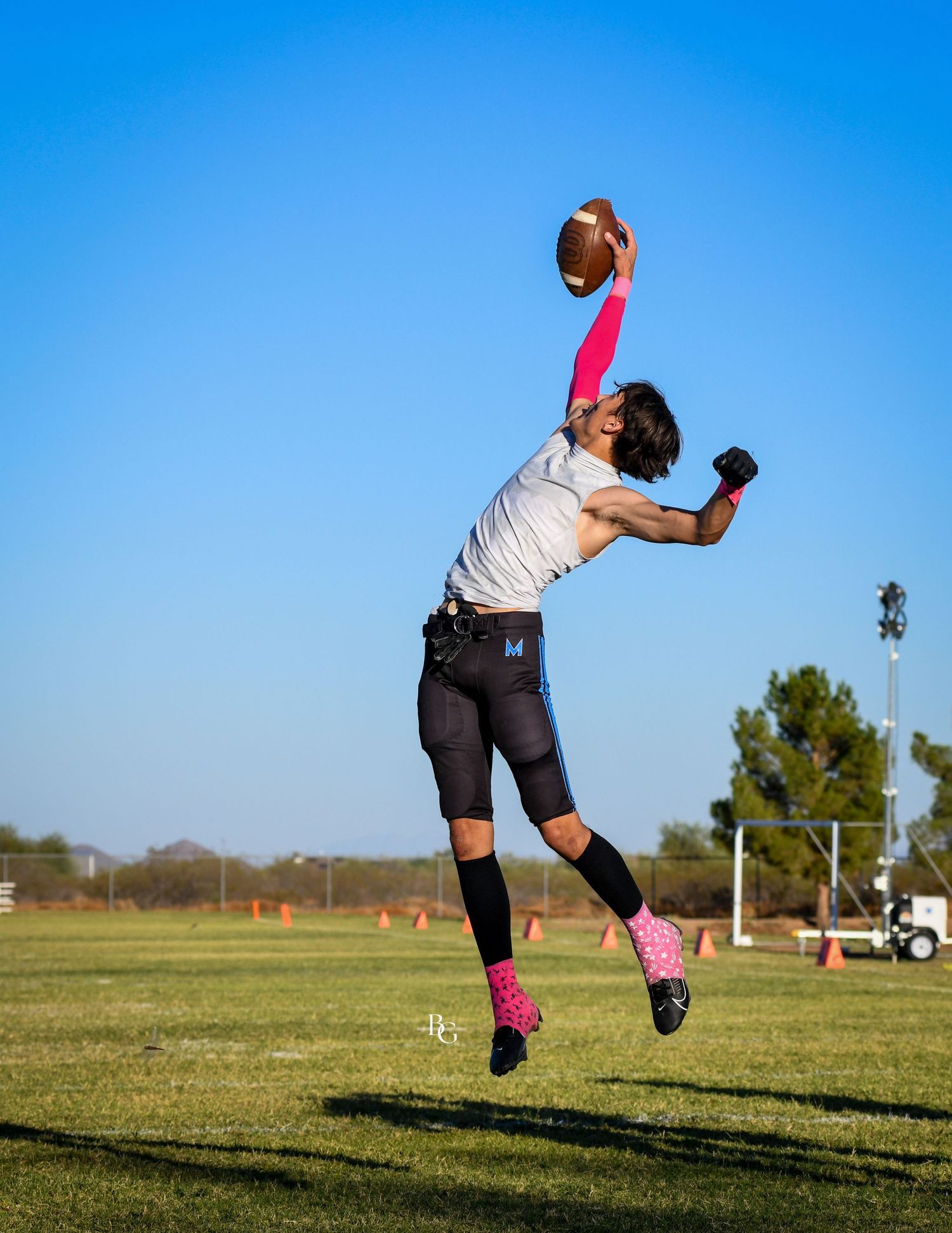 Athlete leaping high to catch football against bright blue sky background.