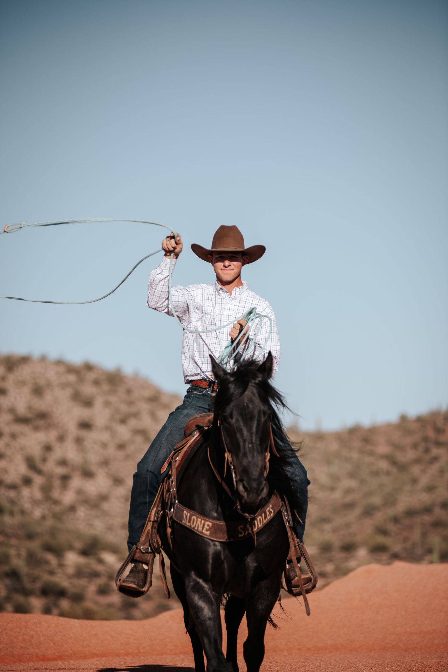 Rider on horseback swinging a lasso against a desert mountain backdrop.