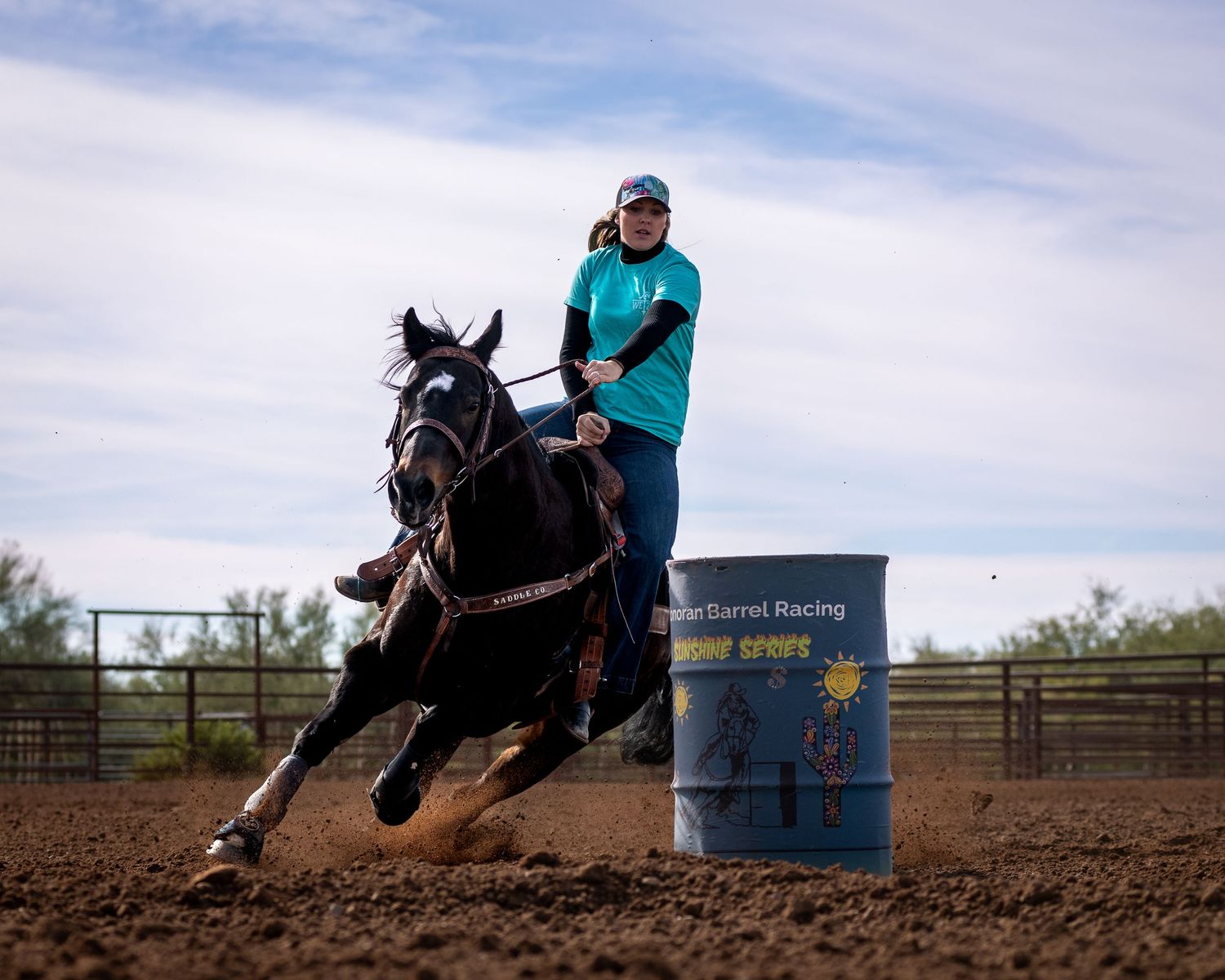 Horse and rider racing around a barrel in a dirt arena during competition.