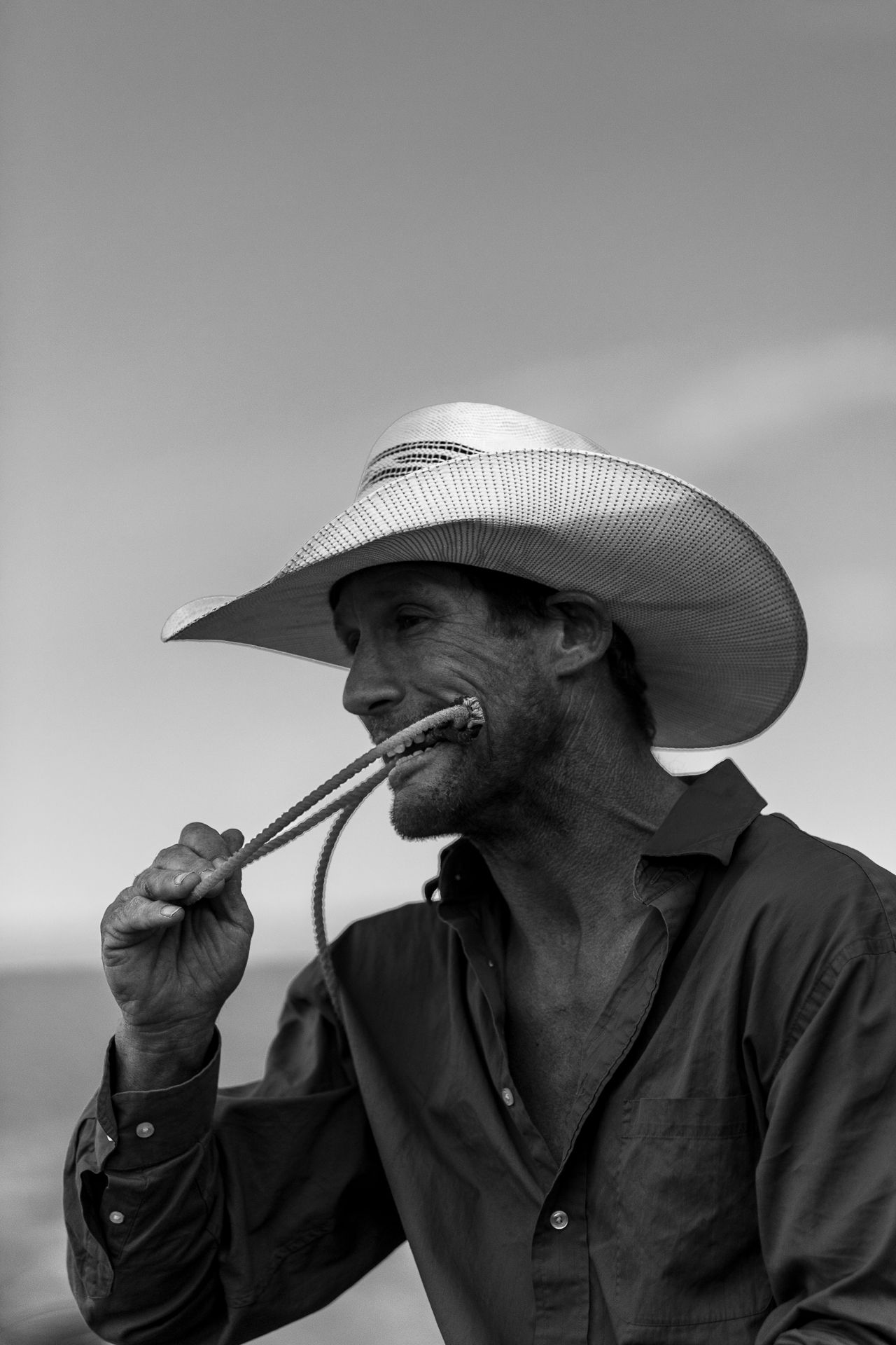 Black and white portrait of someone wearing a cowboy hat holding a rope.
