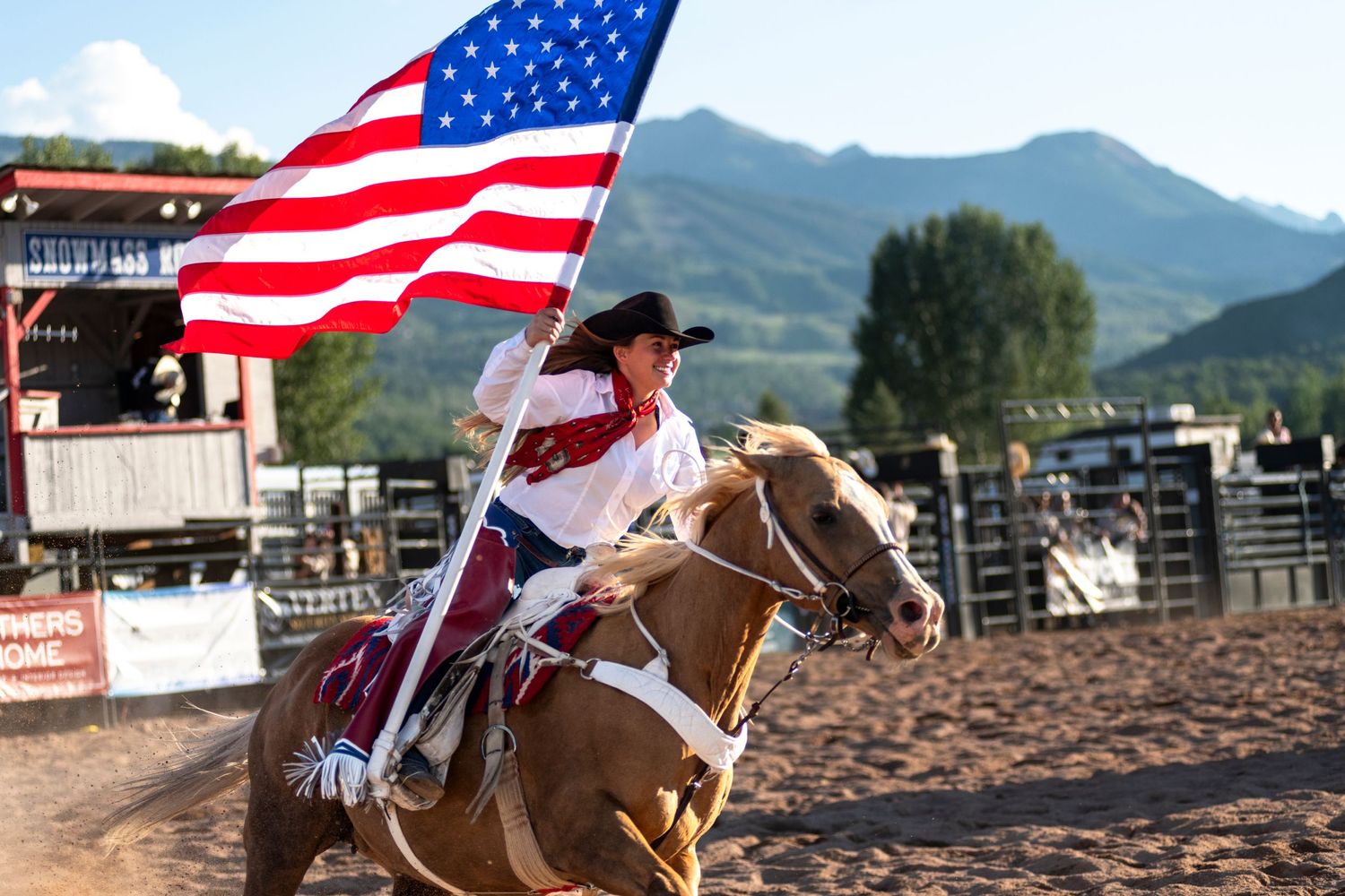 Rodeo rider carrying American flag while galloping through arena.