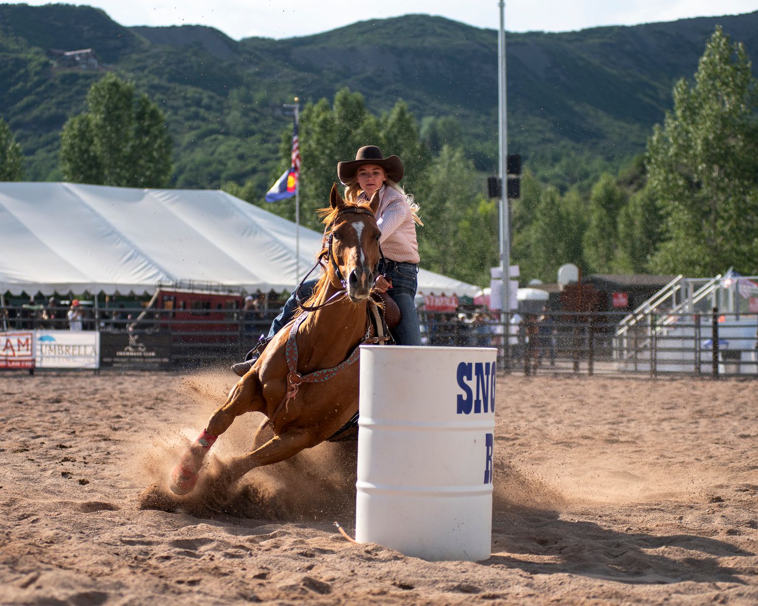 Barrel racing competition at rodeo arena with mountains in background.