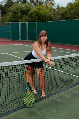 Tennis player relaxes at the net on an outdoor court wearing athletic attire. Senior photo session. Lake Geneva Wisconsin Photographer