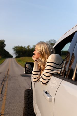 Person leaning out car window on empty rural road during sunny day. Senior photo session. Lake Geneva Wisconsin Photographer