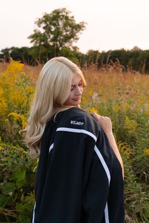 Person wearing black jacket poses in field of golden wildflowers at sunset. Senior photo session. Lake Geneva Wisconsin Photographer
