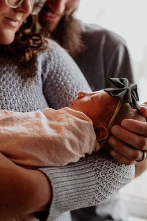 Close-up shot of parents holding sleeping newborn with gray bow accessory.