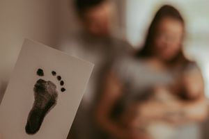 Baby footprint card in focus with blurred family moment in background.