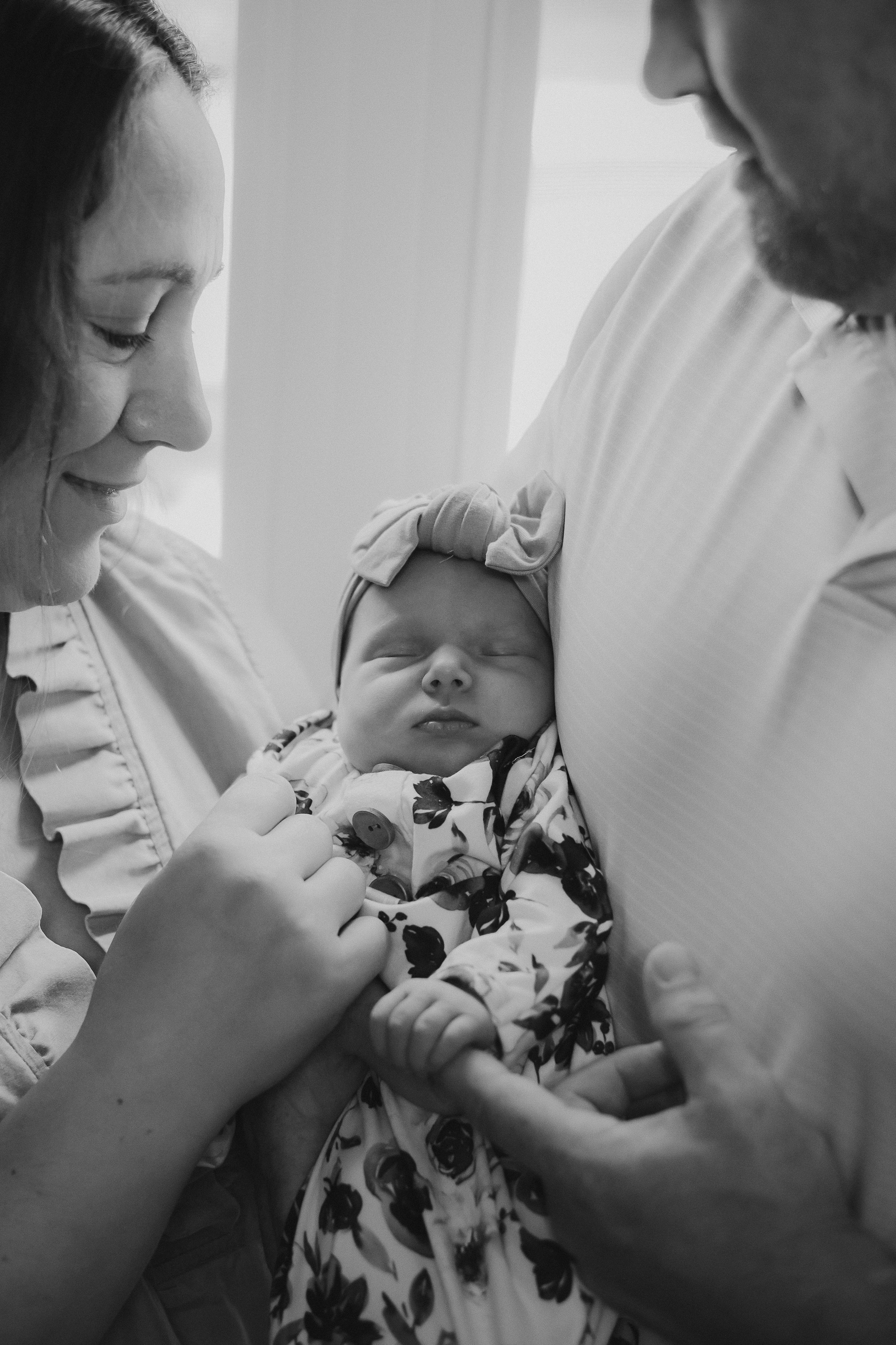 Black and white photo of parents admiring their sleeping newborn baby.