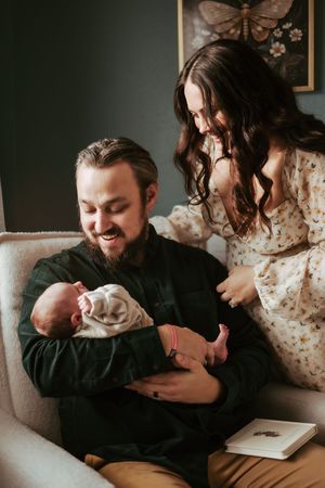 Parents share an intimate moment with their newborn baby while sitting on a beige armchair.