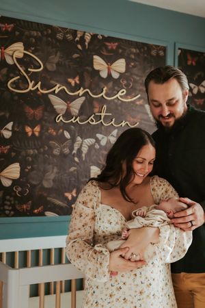 Decorative wall with butterflies serves as backdrop for tender family moment with newborn.