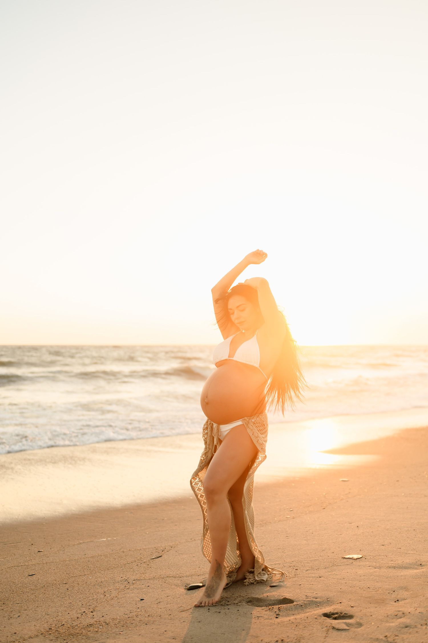 bikini maternity photoshoot during sunset at Oxnard Shores beach of woman in crochet skirt and white bikini by Ventura photographer