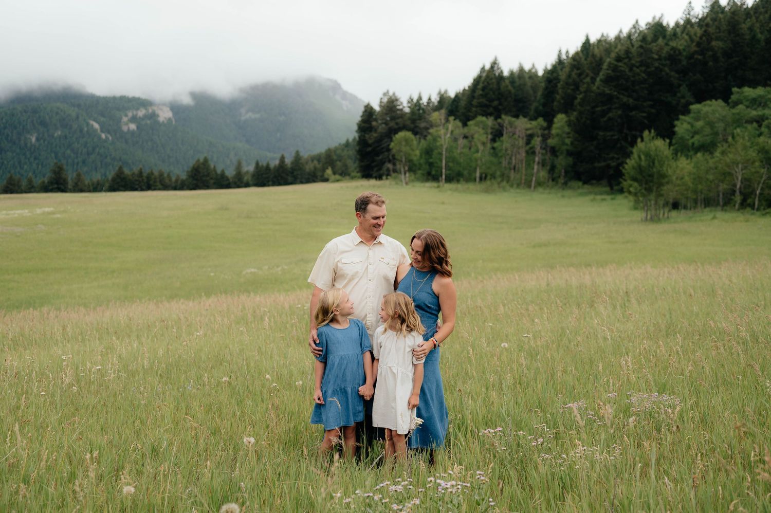 Family of four in blue and white standing in a lush green meadow with misty mountains behind.