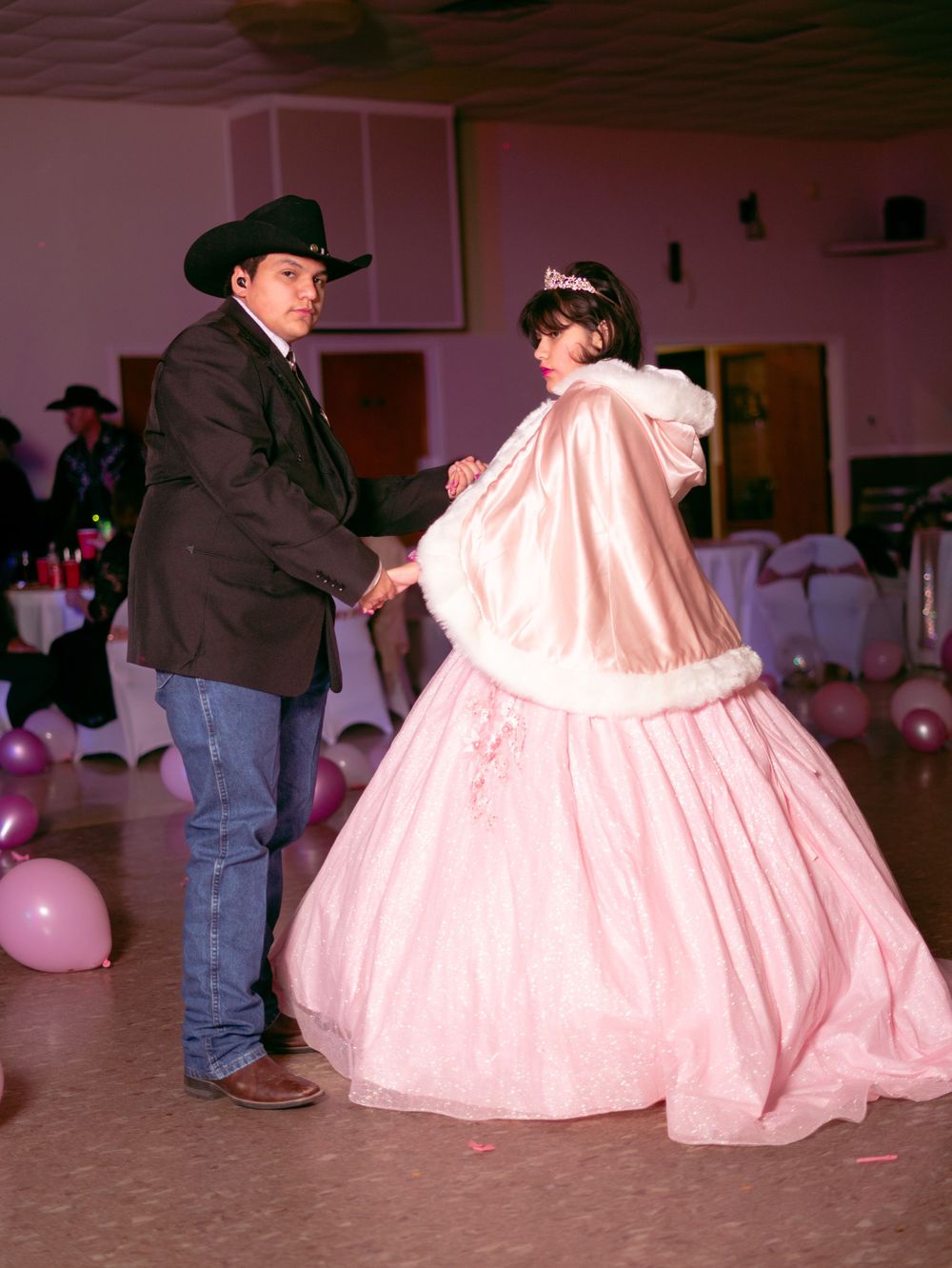 Siblings dancing at quinceañera celebration with woman in pink ballgown and man in western wear.