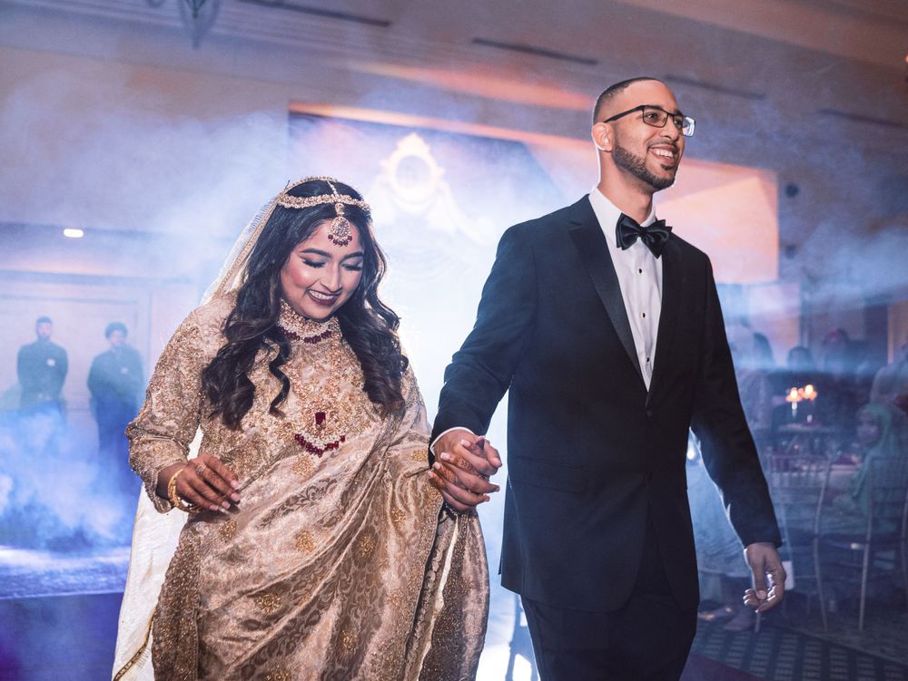 Newlyweds in fusion wedding attire walk through fog-filled reception venue.