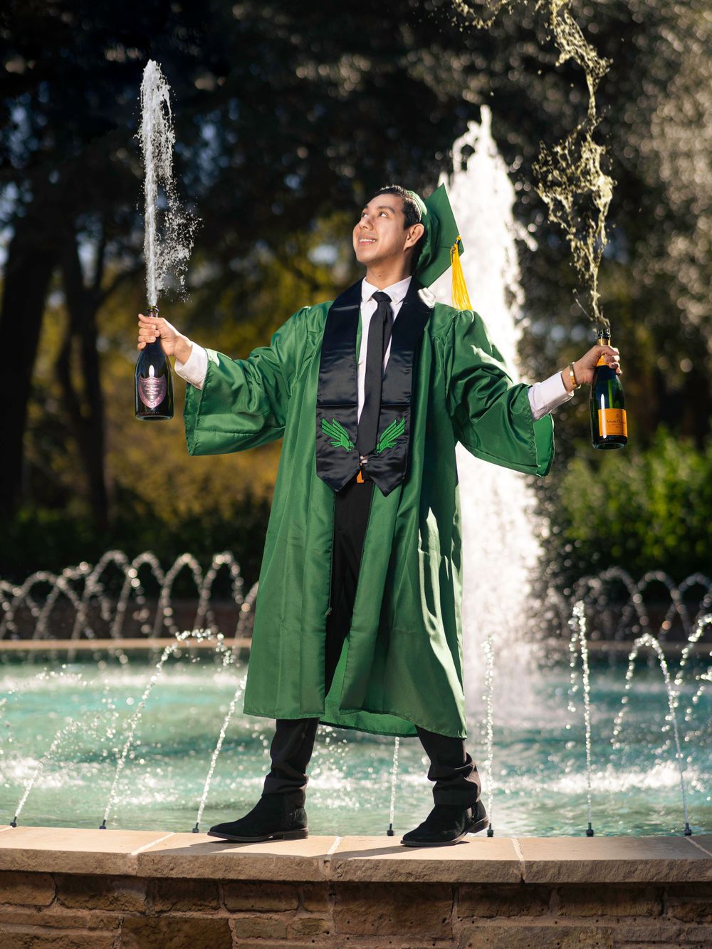 Celebratory graduation photo with champagne bottles spraying in front of fountain.