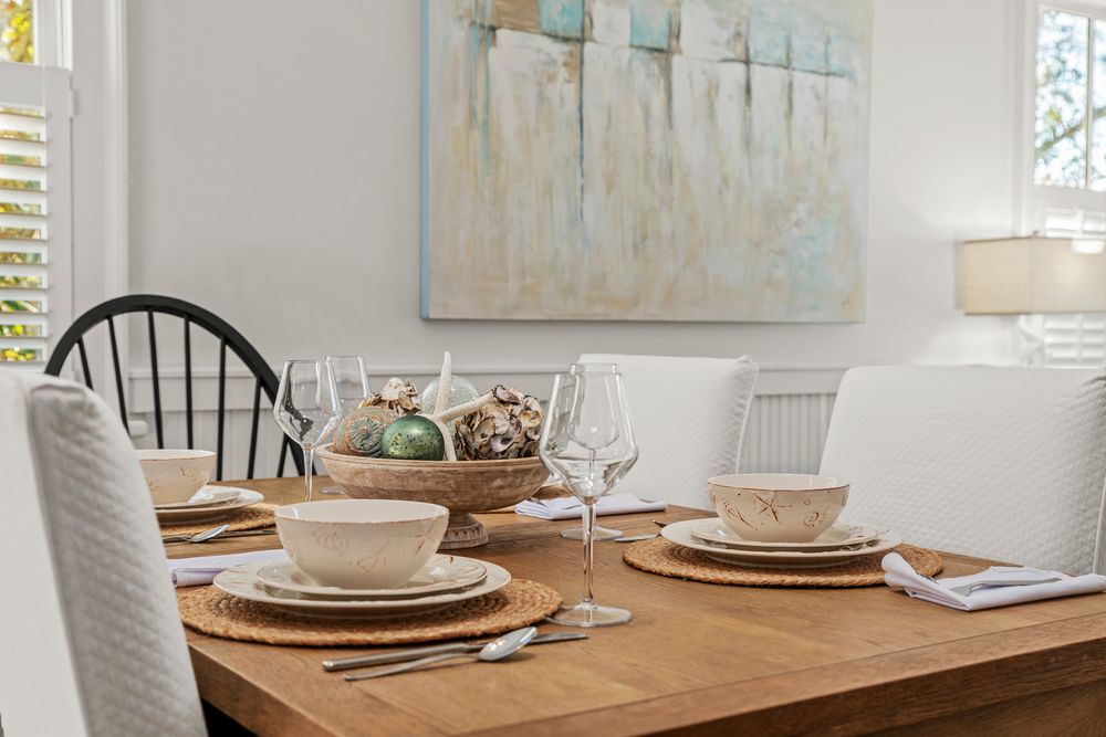 Elegant table setting with white plates and natural decor on wooden dining table next to abstract wall art.