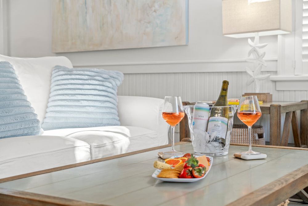 A cozy living room setting with wine glasses and appetizers on a wooden coffee table near light blue throw pillows.