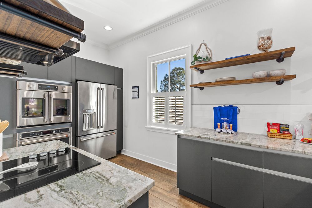 Modern gray kitchen with marble countertops, stainless steel appliances, wood open shelving and plantation window shutters.