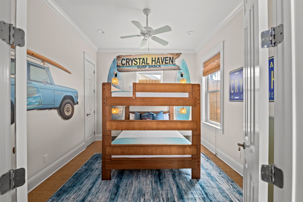 Coastal-themed rooms with bunk beds and nautical decor feature white walls and hardwood floors in a beach house.