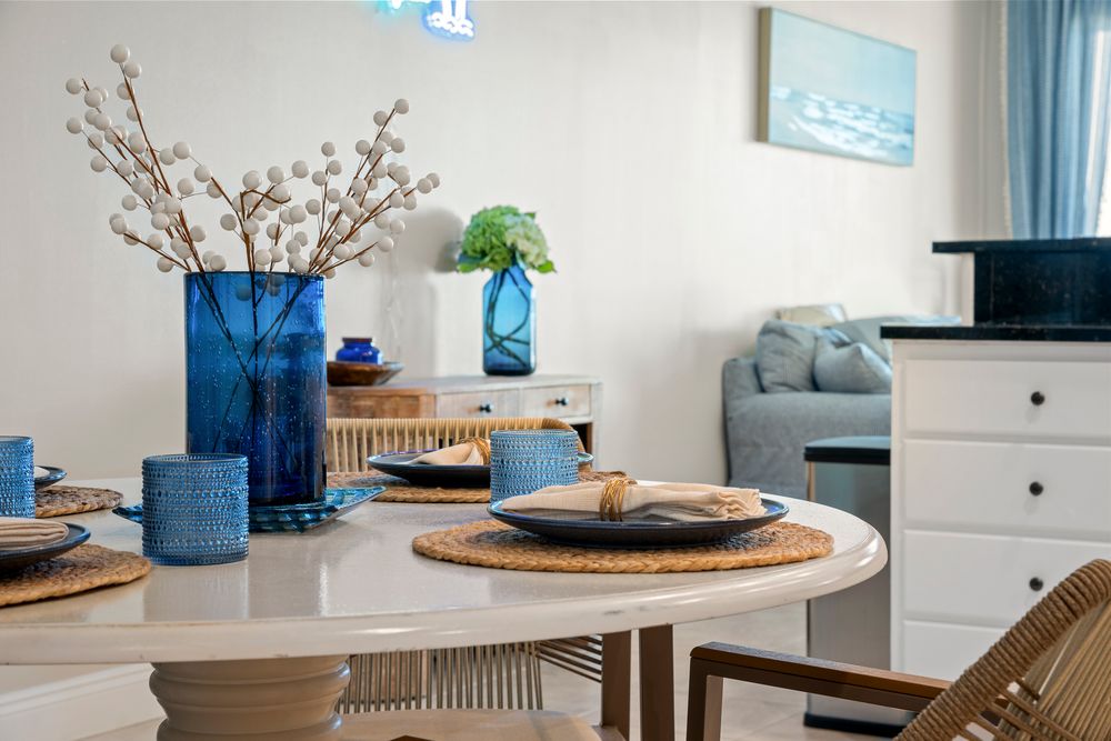 Modern coastal living room features blue accents, natural wood furniture, and beachy wall art in a bright white space.