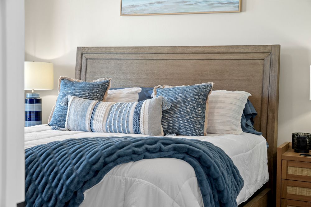 Coastal-themed bedroom with navy blue bedding, driftwood-style furniture, and ocean artwork above the headboard.
