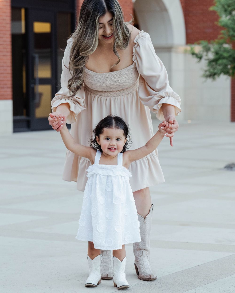 Two figures in matching white and beige outfits standing on sidewalk.