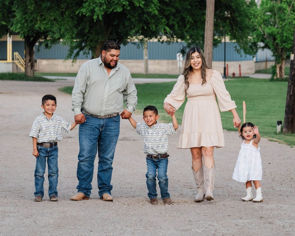 Family dressed in coordinating neutral tones poses together outdoors in a grassy park.