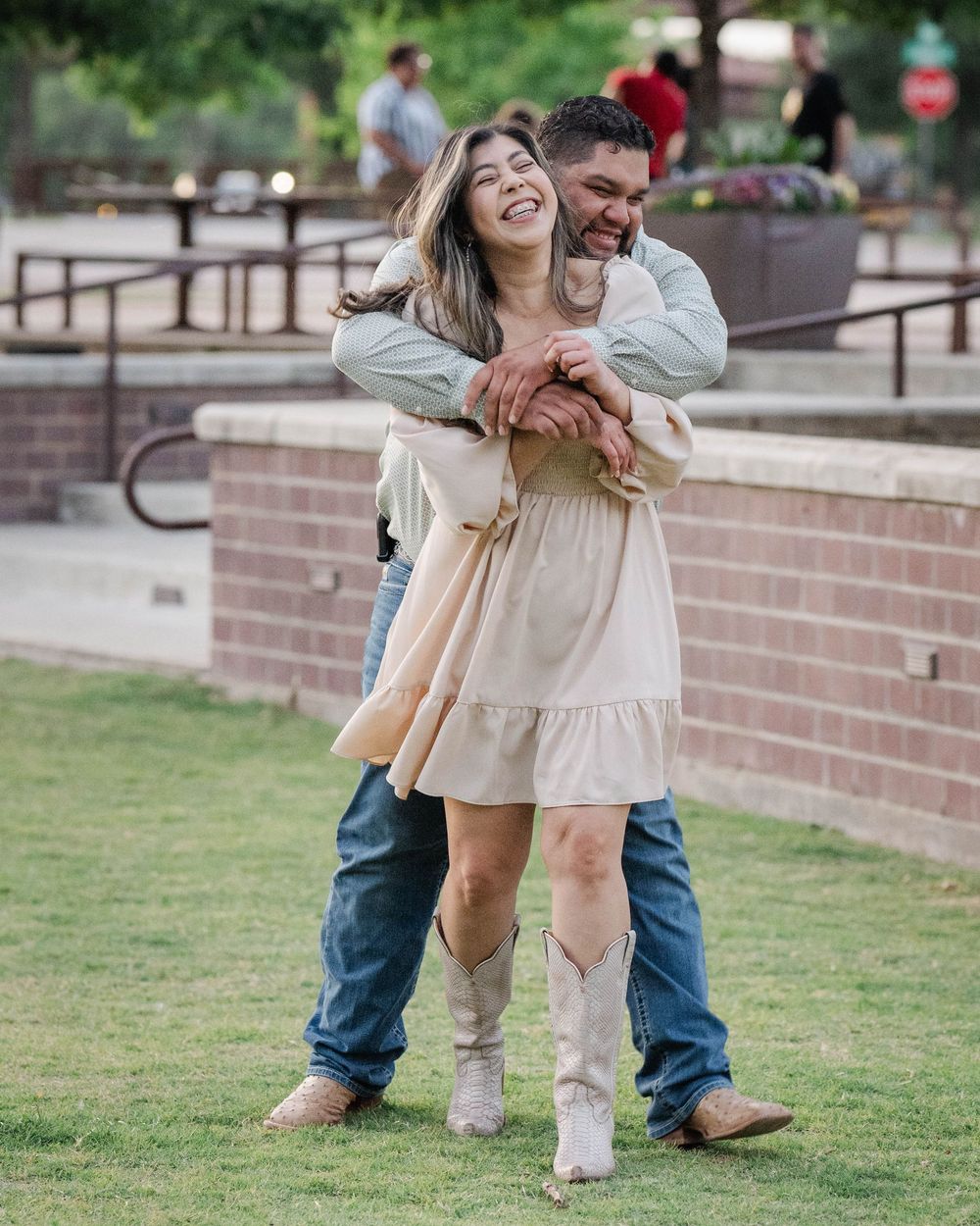 Couple in casual attire embracing and laughing together on a grassy lawn.