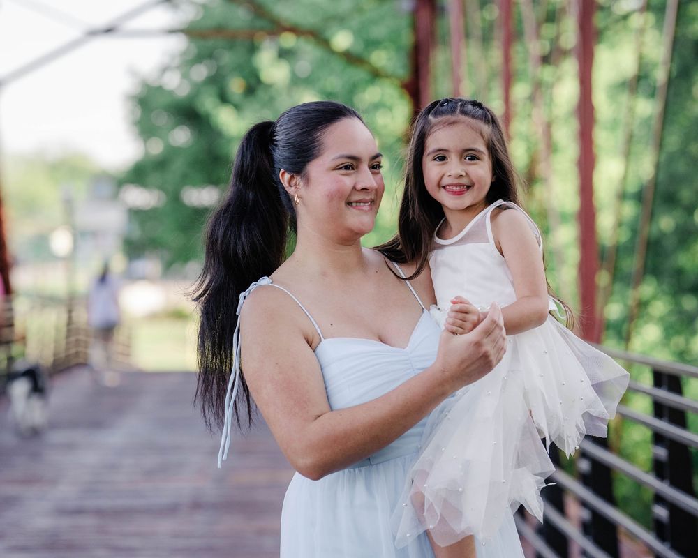 Parent and child in matching white dresses share a joyful moment on a wooden walkway.
