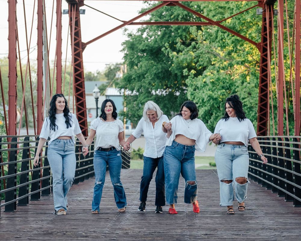 Group of women in casual attire walking together on a rustic red bridge surrounded by trees.