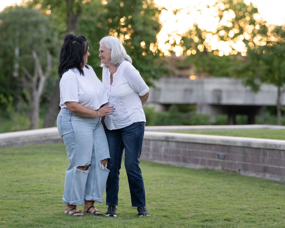 Two people in casual denim and white tops share a tender moment outdoors at sunset.