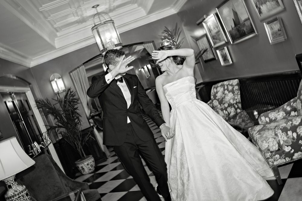 Black and white photo of a bride and groom dancing elegantly in a decorated ballroom during their wedding reception.
