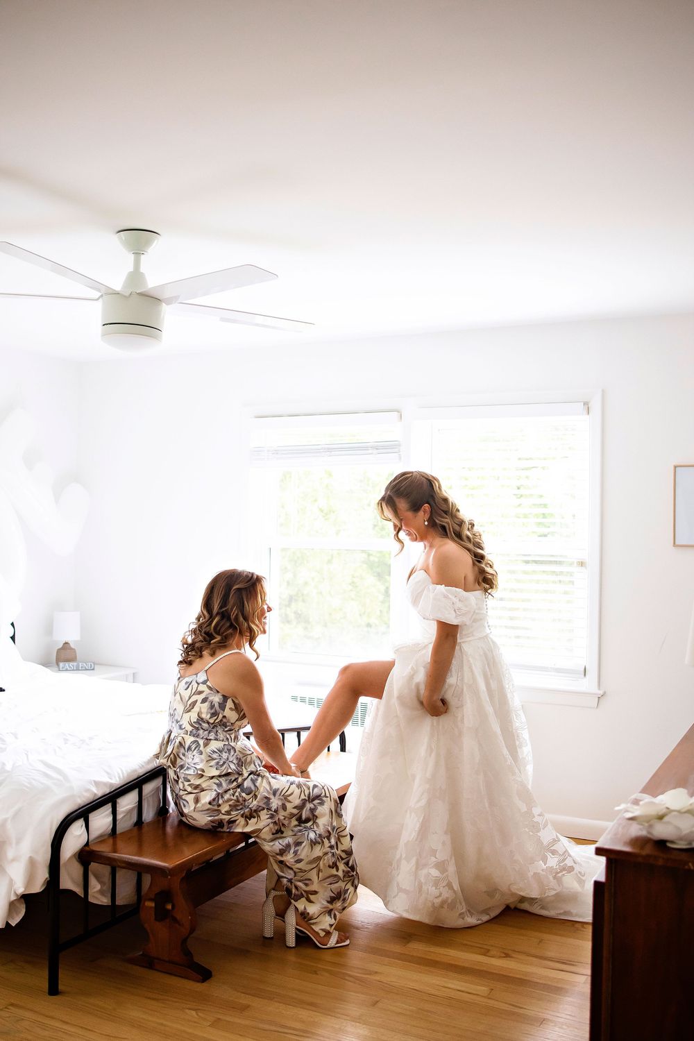 Two people share an intimate moment during wedding preparations in a bright, sunlit room with hardwood floors.
