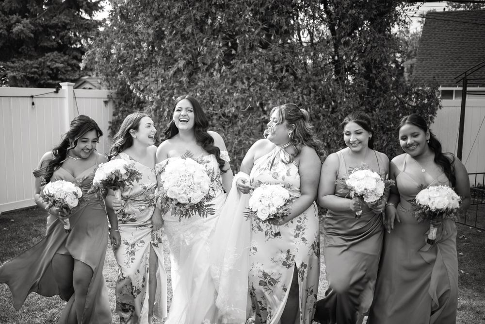 Bridal party in floral and solid dresses pose with bouquets in black and white photography.
