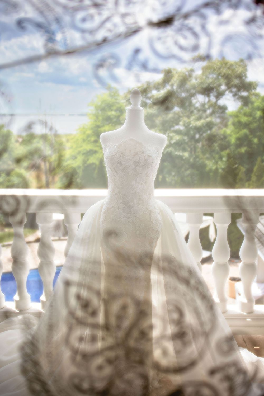 White lace wedding dress on mannequin displayed on balcony through decorative window.