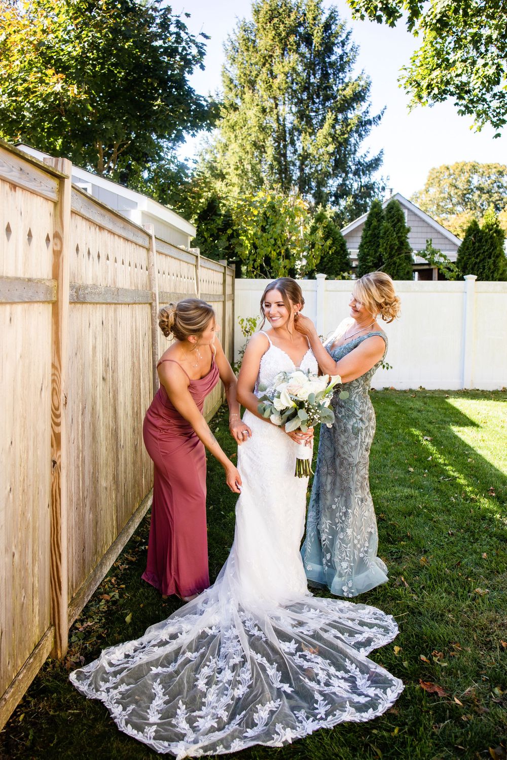 Wedding dress with intricate lace train being adjusted in a backyard setting.